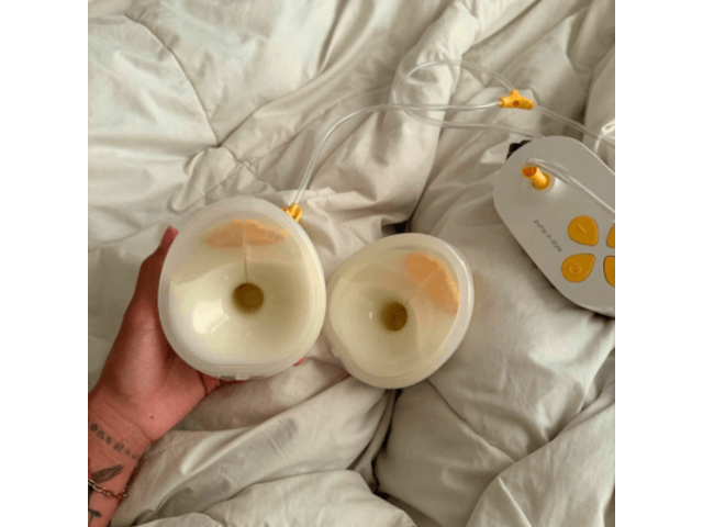 Pump In Style Hands-free breast pump with full collection cups sitting on white down comforter.